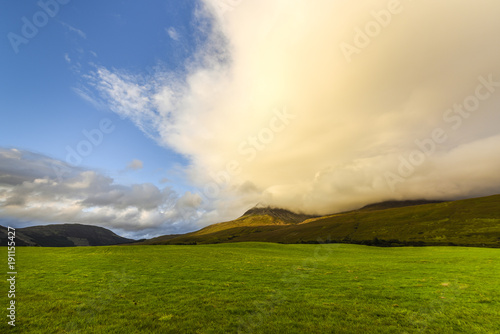 Idyllic meadow with mountains in the background, blue sky and orange clouds in appealing sunset atmosphere, Highlands, Scotland, Great Britain