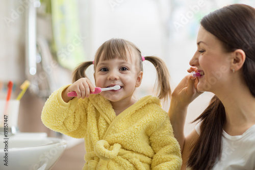 Beautiful mother and kid brushing teeth in bathroom photo