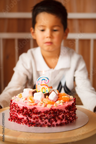 boy sits in front of a cake and makes a wish. the child anticipates blowing out the candles.