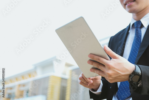 businessman in suit holding touchpad while standing outside building. young asian man using digital tablet for work outdoors © 88studio