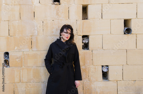 The woman in a black coat against the background of a wall, mourning expression
 and depressions