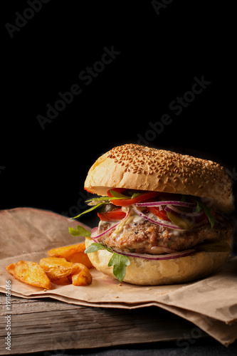 appetizing hamburger with blue onions, tomatoes and greens on a wooden plank