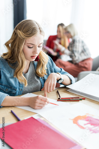 young blonde magazine editor drawing sketches in modern office, colleagues sitting behind