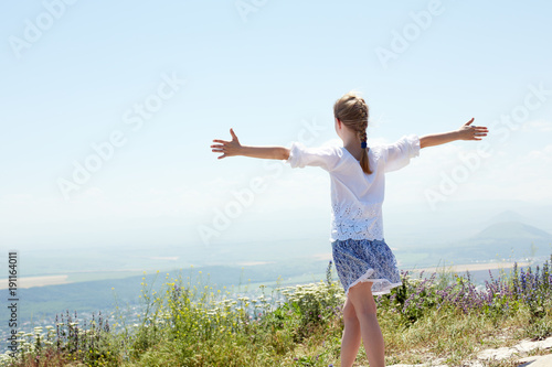 Concept of happiness. Cute happy  child in white blouse on a rock with raised hands and looking to a valley below