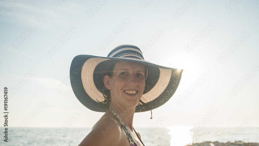 Portrait of a woman with wet hair wearing striped straw hat and swimsuit at the beach