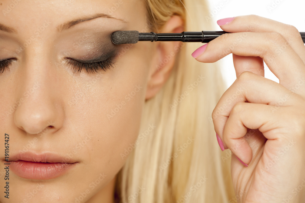 A young blonde woman applying eyeshadow with makeup brush