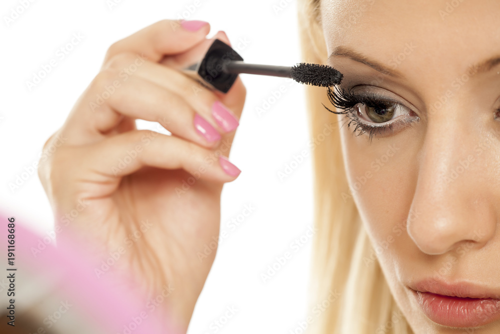 A young blonde woman applying mascara on her eyelashes
