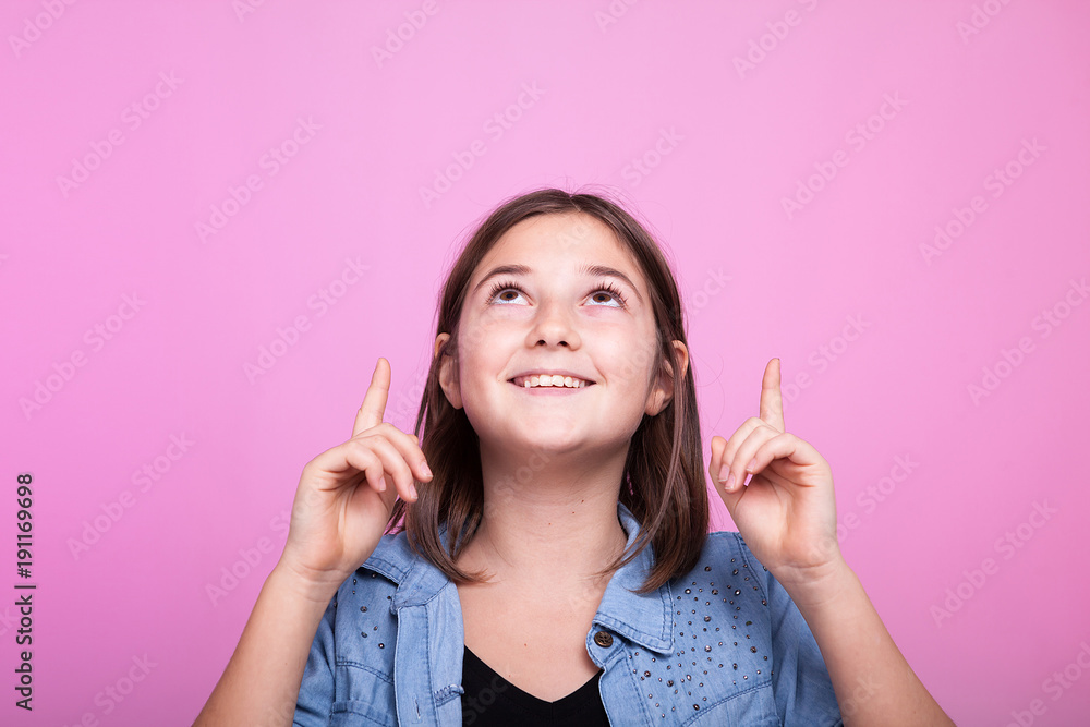 Close up portrait of happy girl poiting up on pink background in studio photo Close up portrait of happy girl poiting up on pink background in studio photo