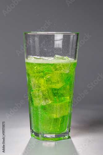 fizzy drink with ice in glass on gray background