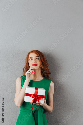 Thinking redhead young woman in green dress holding surprise