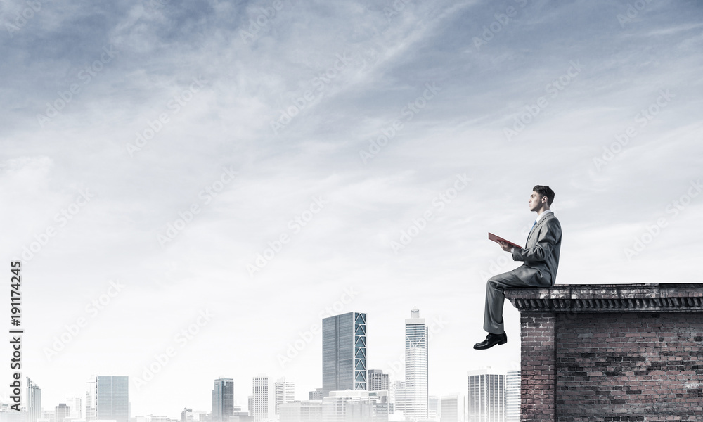 Man on roof edge reading book and cityscape at background Man on roof edge reading book and cityscape at background