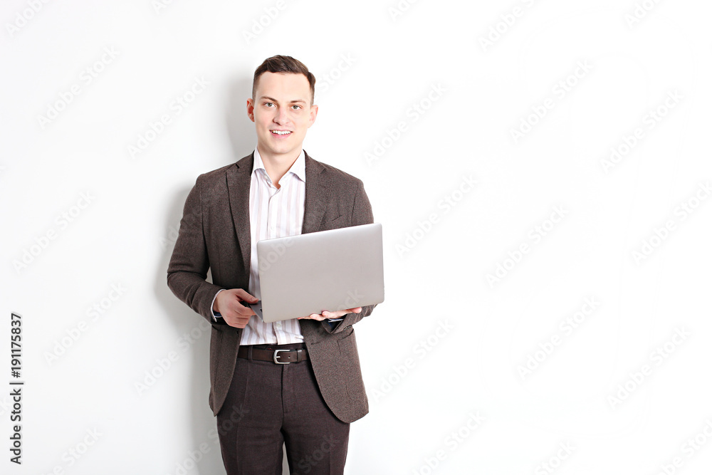 Smiling confident young man, no tie, holding grey laptop device and typing while standing against solid white wall. Wireless internet, wifi, enter password. Shaved, no facial hair. Isolated background Smiling confident young man, no tie, holding grey laptop device and typing while standing against solid white wall. Wireless internet, wifi, enter password. Shaved, no facial hair. Isolated background