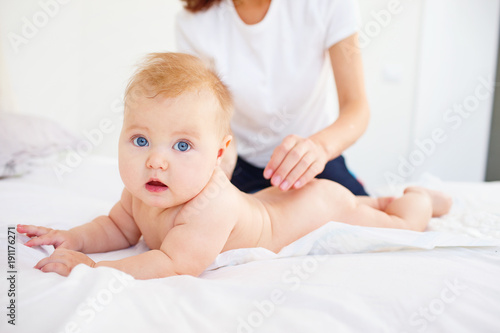 Woman spreading her baby with cream while lying on bed. 