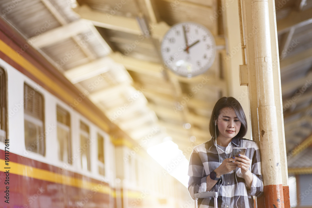 Obraz premium People using a mobile at the train station. Woman standing at train station while listening to music on her smartphone.
