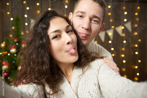 Happy couple taking selfie and having fun in christmas decoration. Dark wooden interior with lights. Romantic evening and love concept. New year holiday.
