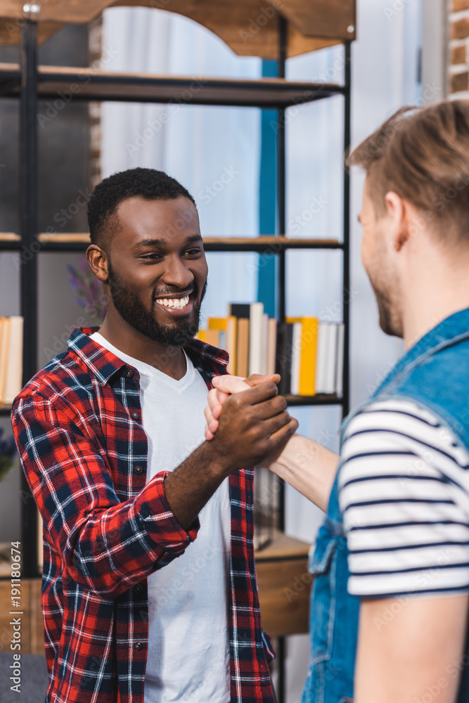 Fototapeta premium cropped shot of young multiethnic men holding hands and smiling each other