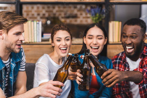 happy young multiethnic friends clinking beer bottles