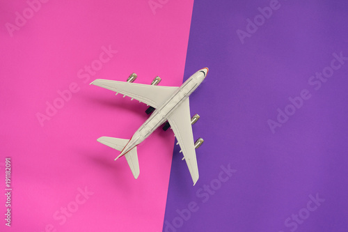 Flat lay design of travel concept with plane on violet and pink background with copy space.