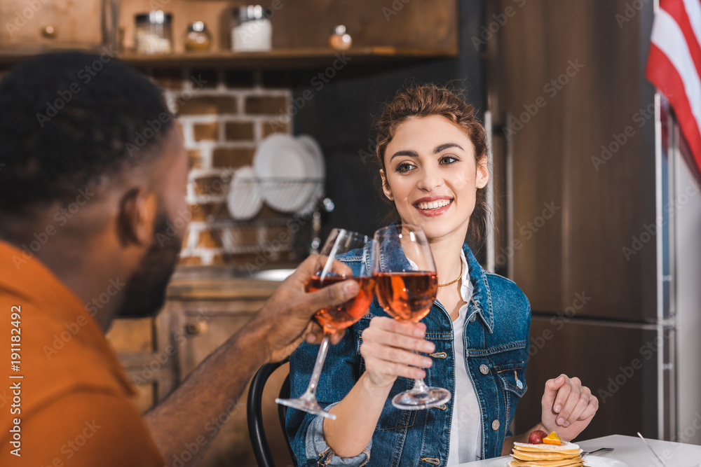 happy young multiethnic couple clinking wine glasses at home