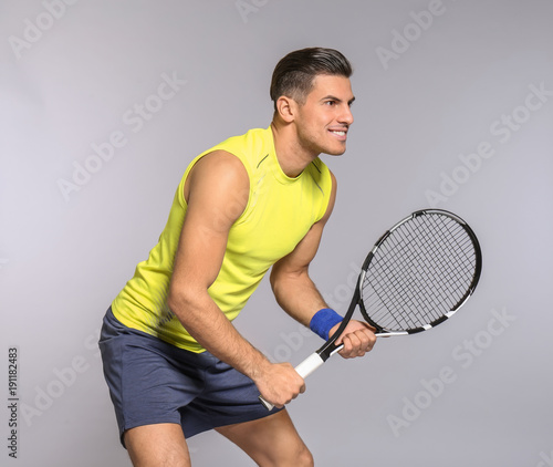 Portrait of handsome man playing tennis against grey background © Africa Studio