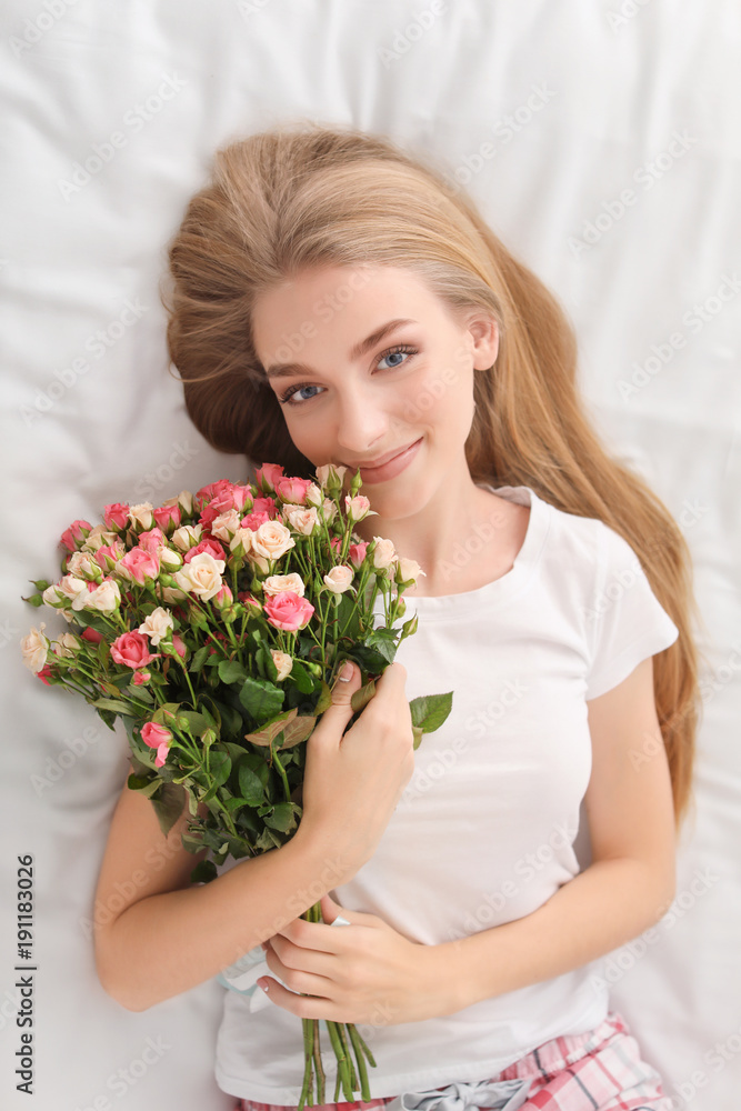 Beautiful young woman with bouquet of roses on bed at home
