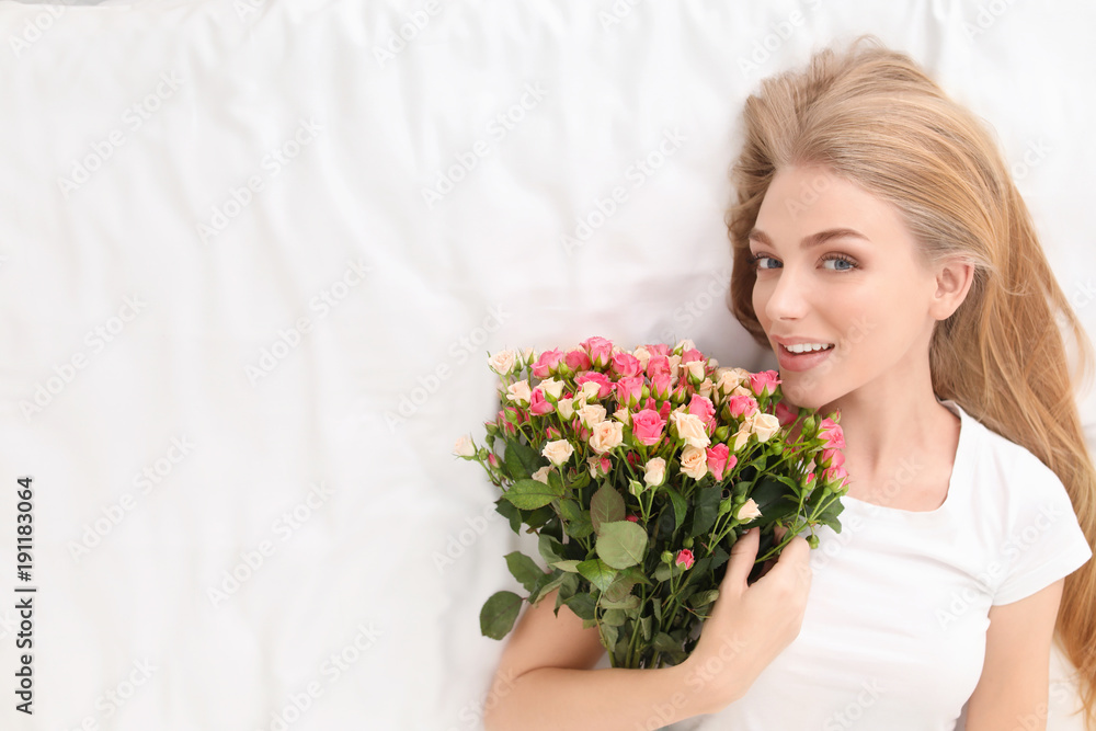 Beautiful young woman with bouquet of roses on bed at home Beautiful young woman with bouquet of roses on bed at home