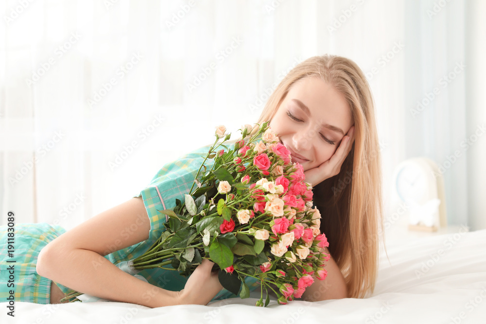 Beautiful young woman with bouquet of roses on bed at home