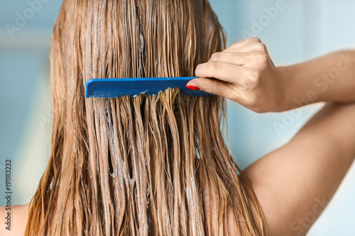 Fotografie Young woman combing hair covered with mask, indoors