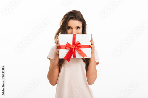 Playful brunette woman in t-shirt hiding behind gift box