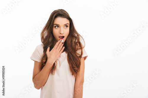 Surprised brunette woman in t-shirt covering mouth and looking away