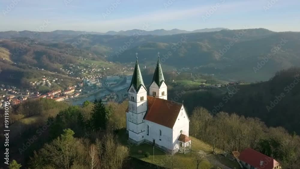 Aerial: Flying round old catholic church on top of the hill on beautiful sunny winter day. Small city by the river in background. Aerial: Flying round old catholic church on top of the hill on beautiful sunny winter day. Small city by the river in background.
