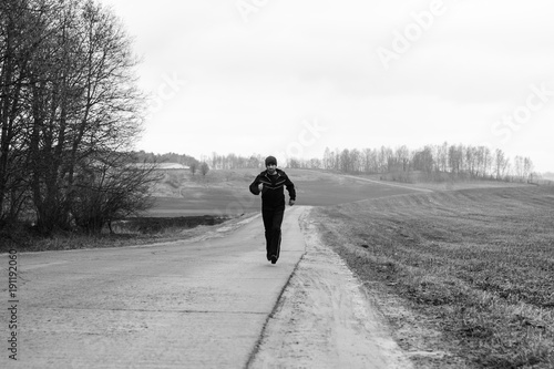 A sportsman is running on a higway in countryside landscape.