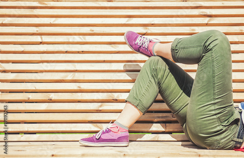Legs of woman in green pants and purple sneaker lying on the bench