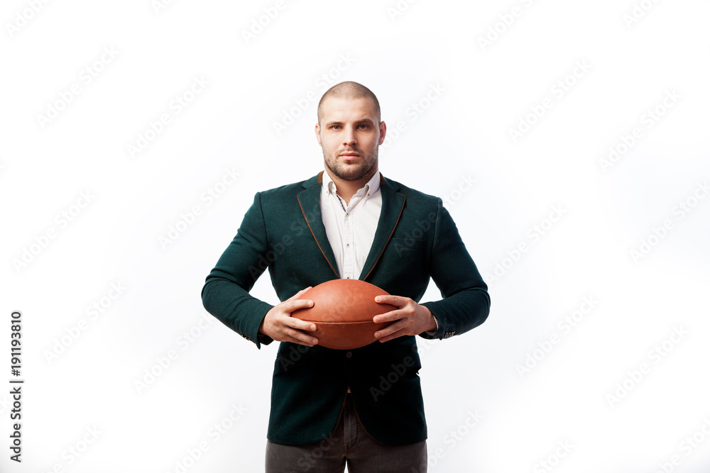 A young bald man in a white shirt, green suit holds a rugby ball poses on a white isolated background A young bald man in a white shirt, green suit holds a rugby ball poses on a white isolated background
