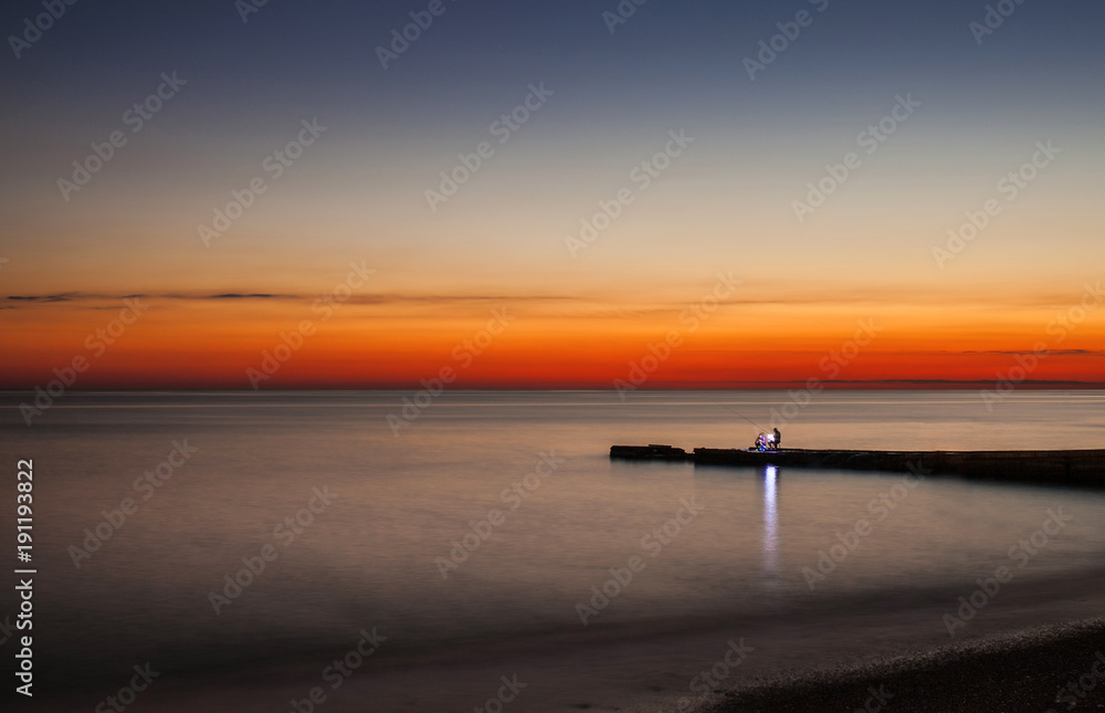 sunset pier. fisherman on the sea coast.
