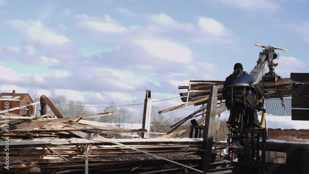 Mechanical arm loader unloads timber scraps from heavy truck at sawmill facility, cold cloudy winter day