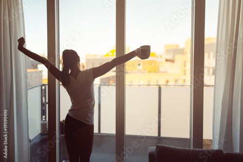 Sleepy woman stretching,drinking a coffee to wake up early in the monday morning sunrise.Starting your day.Wellbeing.Positive energy,productivity,happiness,enjoyment concept.Morning ritual photo