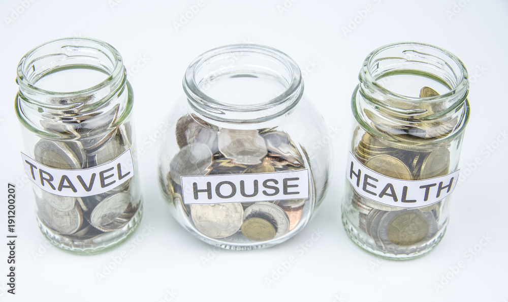 Coins in glass container with travel, house and health label. Selective focus. Coins in glass container with travel, house and health label. Selective focus.