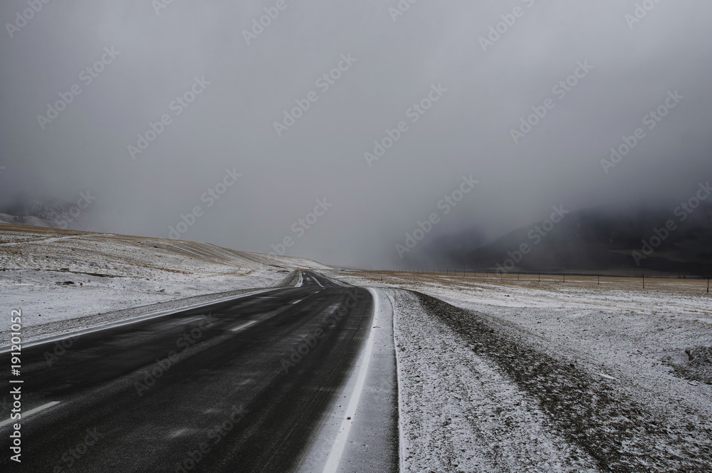 Road asphalt path on a winter snow desert wild mountain valley  at the background of the high peaks under a dramatic storm cloud Chuysky tract Altai Mountains Siberia, Russia