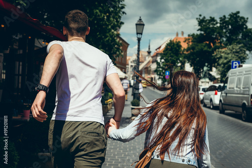 Canvas Print Back view of the two travellers in love holding hands while running along the street in Budapest, Hunagry