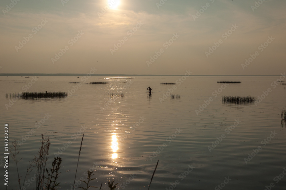 the boy swims in the warm lake on an end of day at the sun in a haze