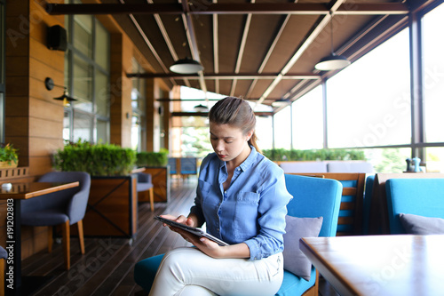 Obraz na plátne Young girl using tablet at restaurant   and sitting in on blue sofa