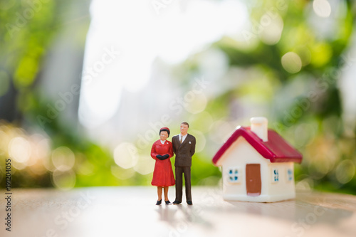 Miniature people, man and woman standing with mini house on green nature background using as relationship and family concept