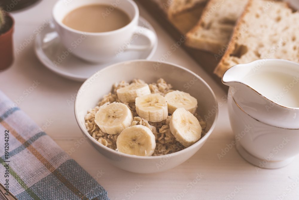 Oatmeal with a banana and coffee with milk for breakfast - close-up, on a light rustic background Oatmeal with a banana and coffee with milk for breakfast - close-up, on a light rustic background