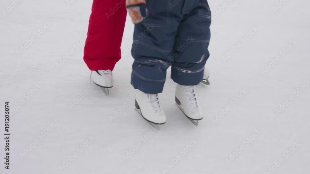 The first steps of a small child on ice skating. Mom teaches skating and holds his child on the ice. Active lifestyle The first steps of a small child on ice skating. Mom teaches skating and holds his child on the ice. Active lifestyle