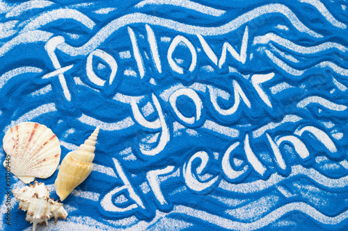 Follow Your Dream inscription on a blue colored sand with waves and sea shells, top view, flat lay photo