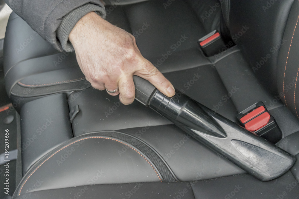 Man vacuuming in the car salon. Hoovering the car. Car vacuum cleaner. Cleaning the auto with an industrial vacuum cleaner. Car vacuum cleaner at a car wash station.