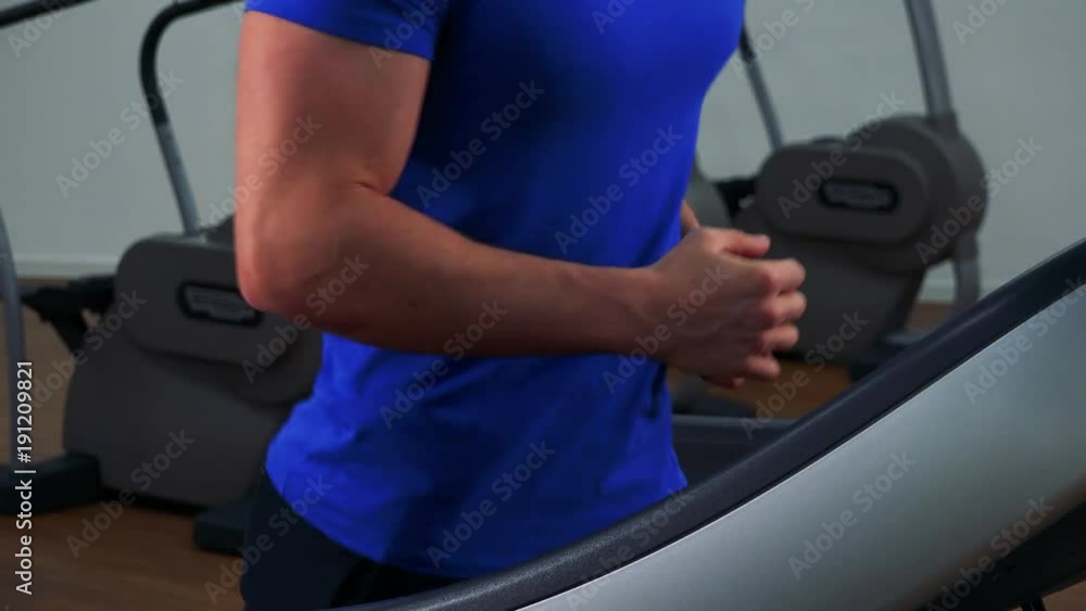 A young fit man walks on a treadmill in a gym - closeup from side A young fit man walks on a treadmill in a gym - closeup from side