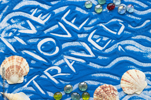 Live Love Travel inscription on a blue colored sand with waves and sea shells, top view flat lay