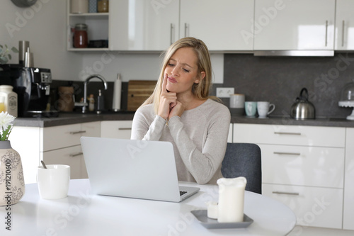 Obraz na plátně Hübsche blonde Frau sitzt an ihrem Laptop und überlegt